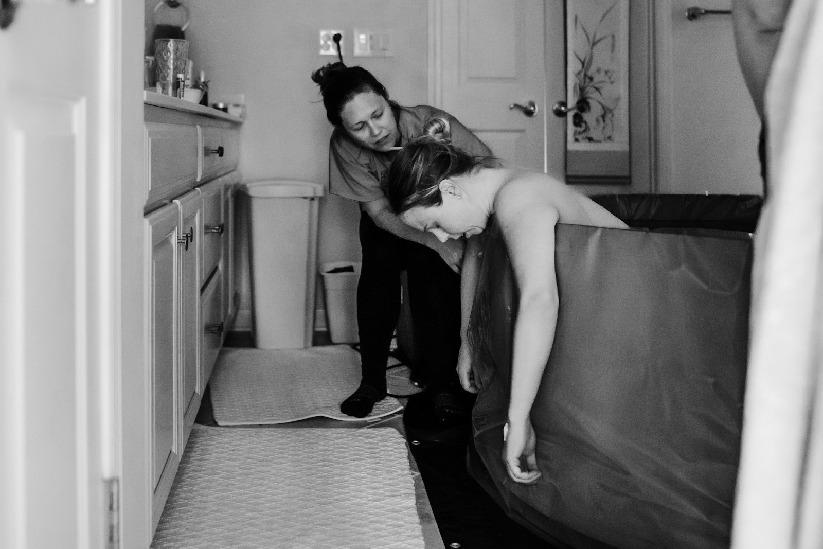 A doula supporting a laboring person who is leaning over a birth pool at home
