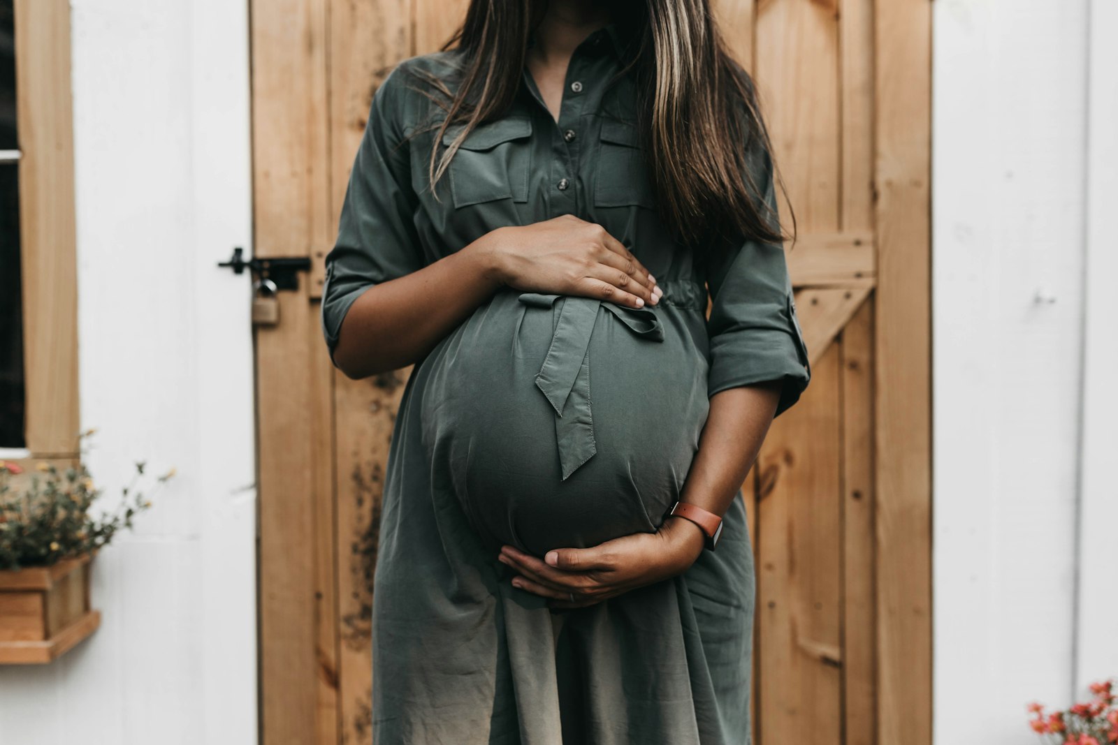 An expecting parent in a green dress resting her hands on her belly