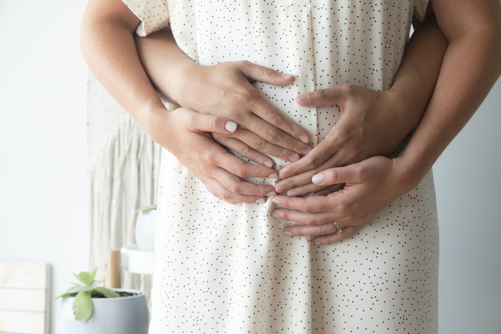 A support person's hands resting over an expecting parent's hands on their pregnant belly