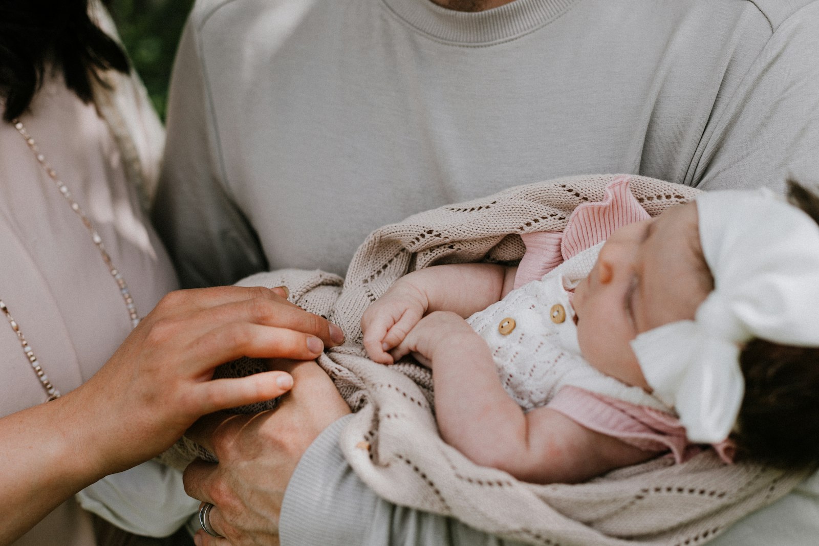 A parent cradling a sleeping newborn wrapped in a knit blanket