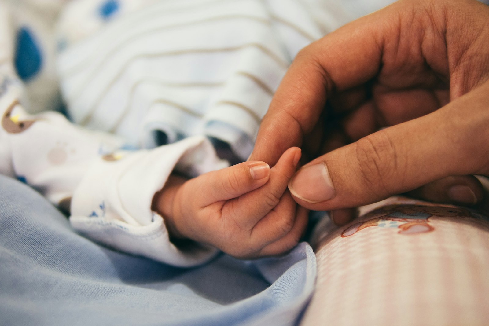 An adult's hand gently holding a newborn's tiny fingers